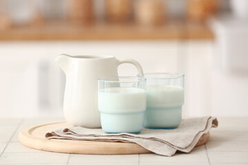 Wooden board with ceramic jug and glasses of milk on white tile table