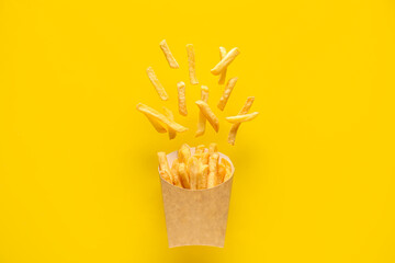 Paper box with tasty french fries on yellow background