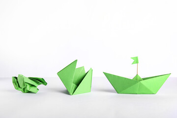 Green origami boat with flag, flower and crumpled paper on white background