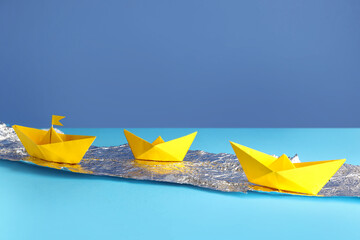 Yellow origami boats with foil on color background