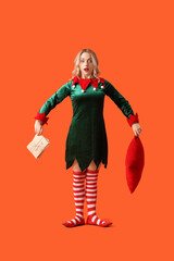 Shocked young woman dressed as elf with pillow and letters to Santa on orange background