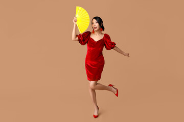 Beautiful young happy Asian woman with fan on brown background. Chinese New Year celebration