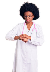 Young african american woman wearing doctor coat and stethoscope checking the time on wrist watch, relaxed and confident