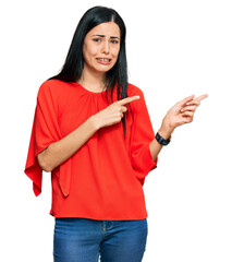 Beautiful young woman wearing casual clothes pointing aside worried and nervous with both hands,...
