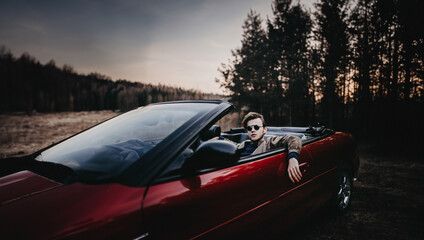 cool man in sunglasses in a red convertible in nature, a rich arrogant man.