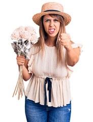 Young beautiful woman wearing hat holding bouquet of flowers annoyed and frustrated shouting with anger, yelling crazy with anger and hand raised