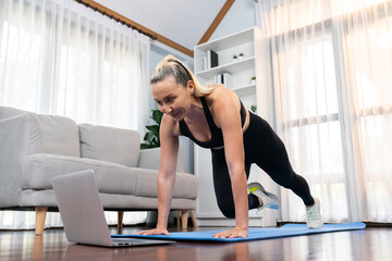 Athletic and active senior woman doing exercise on fit mat with plank climbing at home exercise...