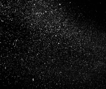 Freezing falling snowflakes or stardust in air on black background for overlay blending mode. Stopping the movement of white powder on a dark background, selective focus