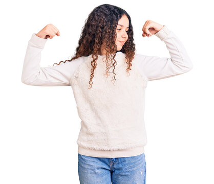 Beautiful kid girl with curly hair wearing casual clothes showing arms muscles smiling proud. fitness concept.