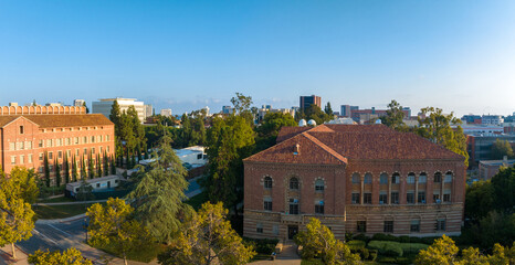 Aerial view of the University of Southern California campus, showcasing historic red-brick buildings, lush greenery, and a scenic city backdrop under a clear blue sky.