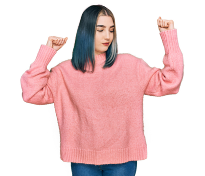 Young modern girl wearing pink wool winter sweater showing arms muscles smiling proud. fitness concept.