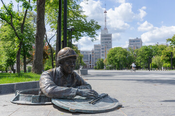 a bronze statue of worker coming out from the manhole on the ground of freedom square in kharkiv...