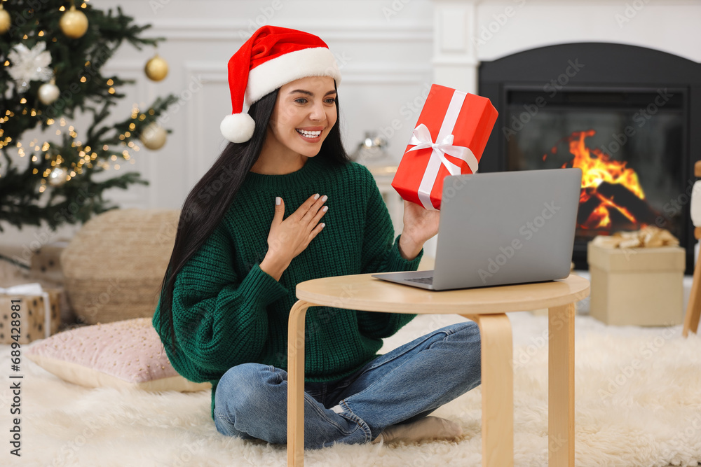 Sticker Celebrating Christmas online with exchanged by mail presents. Smiling woman in Santa hat thanking for gift during video call at home