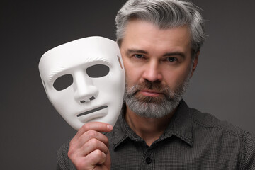 Multiple personality concept. Man with mask on dark grey background - obrazy, fototapety, plakaty