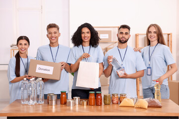 Portrait of volunteers with donation box, paper bag and food products at table in warehouse