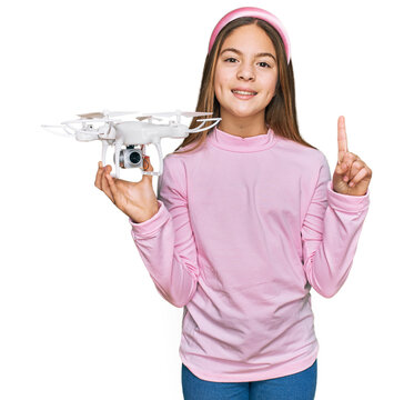 Beautiful brunette little girl using drone surprised with an idea or question pointing finger with happy face, number one