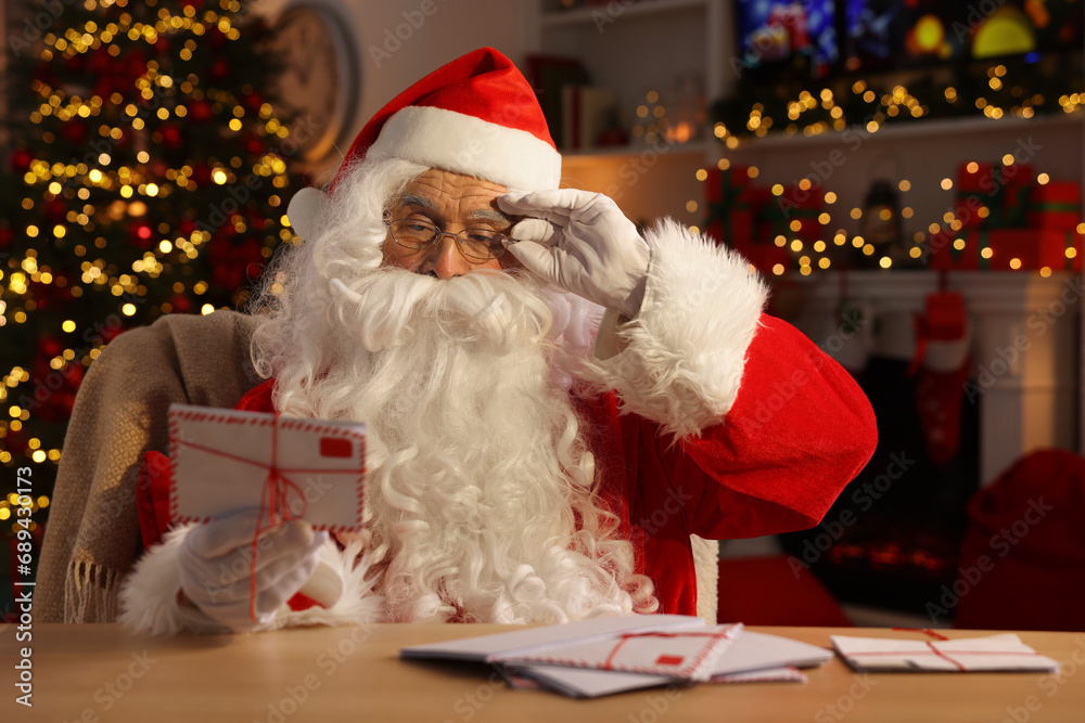 Poster Santa Claus holding letter at table in room decorated for Christmas