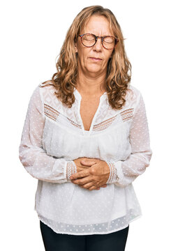 Middle age blonde woman wearing casual white shirt and glasses with hand on stomach because nausea, painful disease feeling unwell. ache concept.