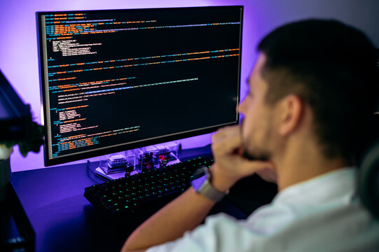 Successful male programmer sits in front of computer screen with programming code abstract technology background of software developer and computer script, working on web resource development