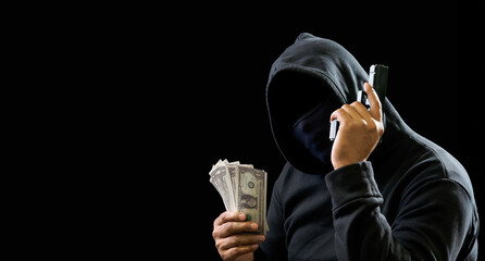 Portrait man thief wearing a black hood shirt, standing hand holding gun and money cash threaten,...