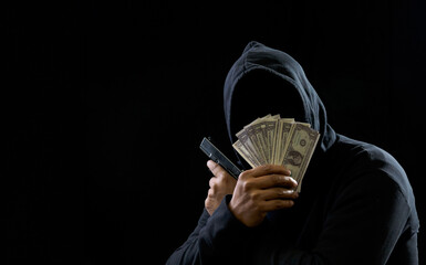 Portrait man thief wearing a black hood shirt, standing hand holding gun and money cash threaten,...