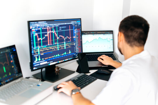 Successful male trader sitting at desk at home office monitoring stock market looking at monitors analyzing price flow, risks and prospects. Stock trading, cryptocurrency concept