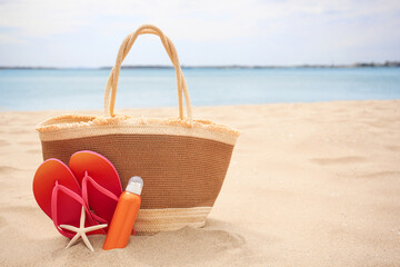 Straw bag, flip flops, starfish and sunscreen on beach, space for text