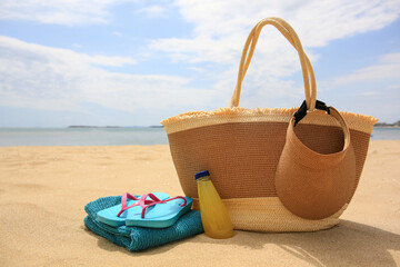 Beach accessories and bottle of refreshing drink on sand near sea, space for text