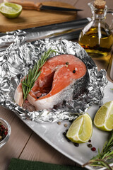 Aluminum foil with raw salmon, lime slices, rosemary and spices on wooden table