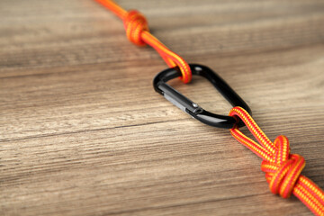 One metal carabiner with ropes on wooden table, closeup. Space for text