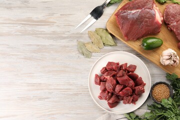 Pieces of raw beef meat, spices and products on light wooden table, flat lay. Space for text