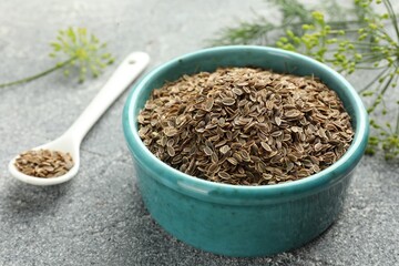Bowl of dry seeds, spoon and fresh dill on grey table, closeup