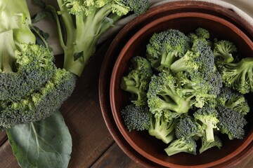 Bowl with fresh raw broccoli on wooden table, flat lay