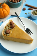 Piece of delicious pumpkin pie with hazelnuts, seeds and fork on light blue wooden table, above view