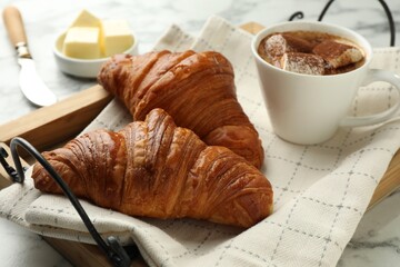 Tasty croissants served with cup of hot drink on white marble table, closeup