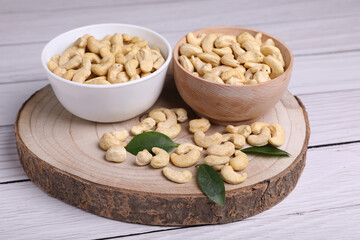 Tasty cashew nuts and green leaves on light wooden table
