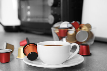Cup of coffee and capsules on light grey table
