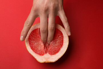 Woman touching half of grapefruit on red background, top view. Sex concept - obrazy, fototapety, plakaty