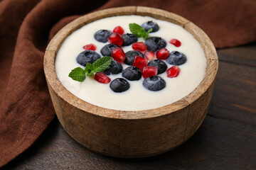 Bowl of delicious semolina pudding with blueberries, pomegranate and mint on wooden table, closeup