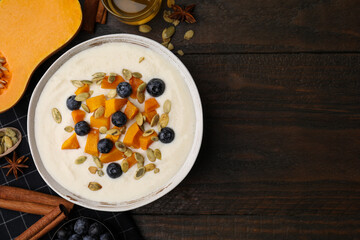 Bowl of delicious semolina pudding with blueberries, pumpkin and ingredients on wooden table, flat lay. Space for text