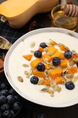 Bowl of delicious semolina pudding with blueberries, pumpkin and seeds on table, closeup