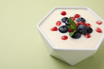 Bowl of delicious semolina pudding with blueberries, pomegranate and mint on light green background, closeup. Space for text