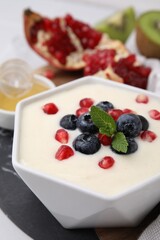 Bowl of delicious semolina pudding with blueberries, pomegranate and mint on table, closeup