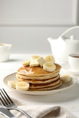 Delicious pancakes with bananas, honey and butter on white wooden table. Space for text