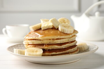 Delicious pancakes with bananas, honey and butter on white wooden table, closeup