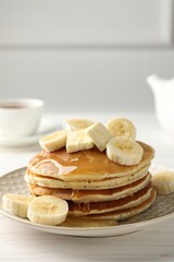 Delicious pancakes with bananas, honey and butter on white wooden table. Space for text