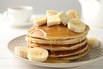 Delicious pancakes with bananas, honey and butter on white wooden table, closeup