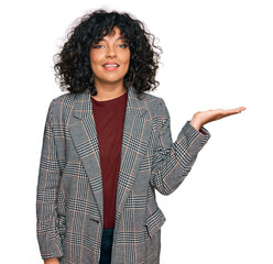 Young hispanic woman wearing business clothes smiling cheerful presenting and pointing with palm of hand looking at the camera.