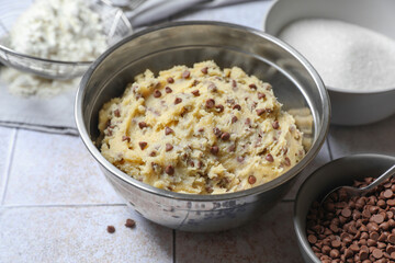 Chocolate chip cookie dough in bowl and ingredients on table, closeup