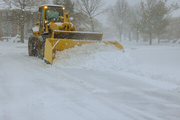In midst of heavy snowstorm, snowplow truck removes snow from car parking lot